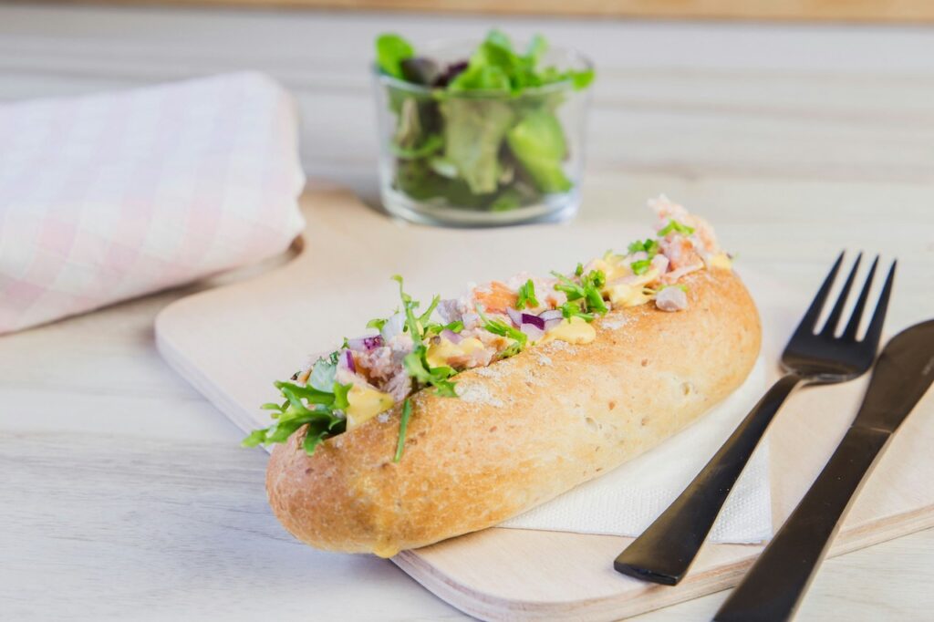 Frisches Baguette mit saftigem Belag aus Gemüse und Kräutern, liebevoll serviert mit knackigem Salat im Hintergrund.